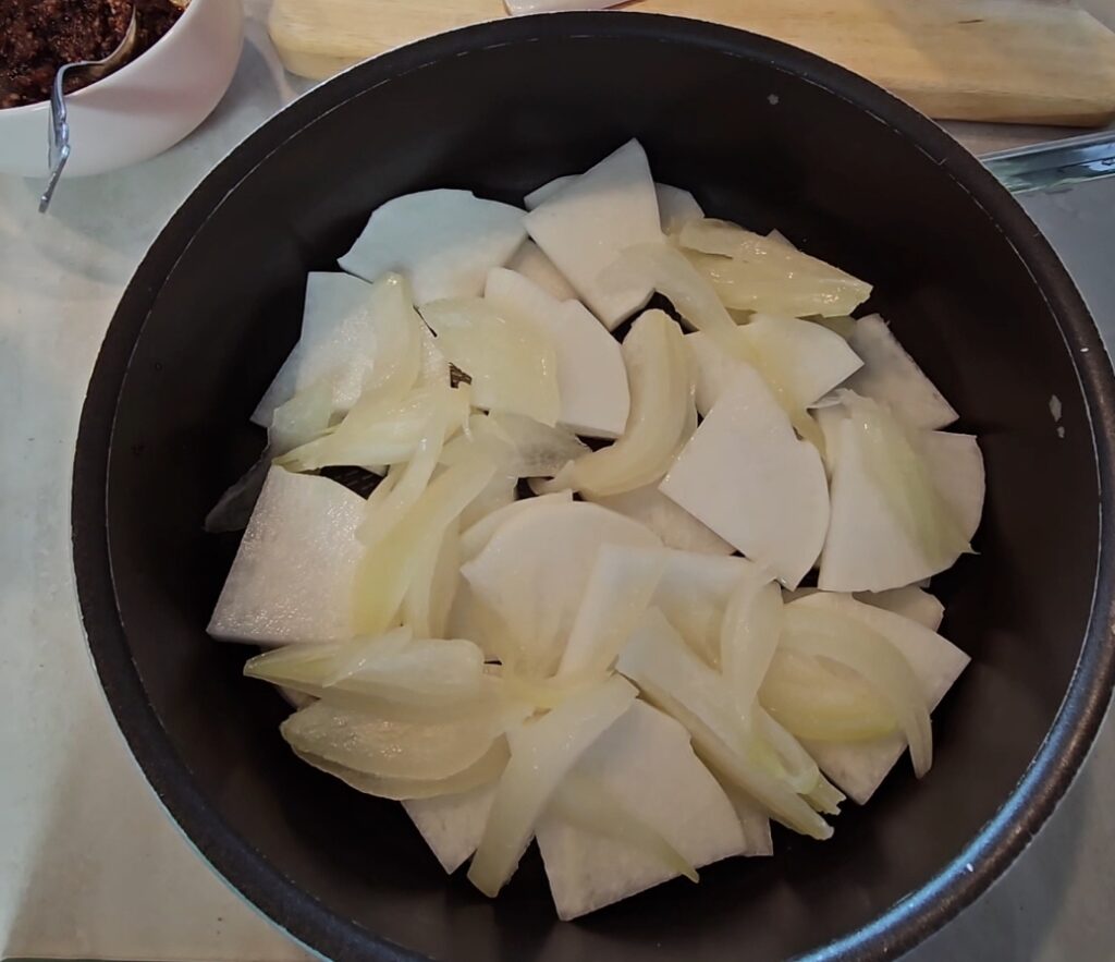 韓国料理。サバの煮物。具材をなべに入れる画像。たまねぎ